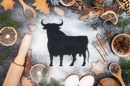 Bull symbol of 2021 painted on flour. Christmas tree, cookies, spices on black background. New Year greeting cardの写真素材