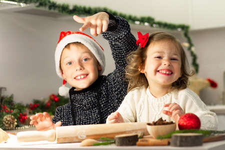 Little cute girl 2-4 with a red bow and boy 7-10 in a Christmas cap make gingerbread cookies in the New Years kitchen.の写真素材