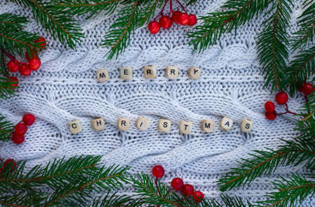 Letters Merry christmas with branches of a Christmas tree and red berries on a white knitted background. Top view.の写真素材