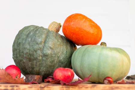Three pumpkins, apples and autumn leaves lying on a wooden table top on a white backgroundの写真素材