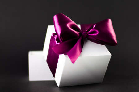 White gift box with lilac ribbon on black, dark background