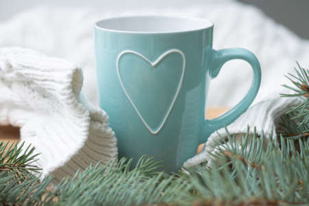 White knit sweater with a mint mug with a heart near the branches of a Christmas tree. Merry Christmas and Happy New Year concept.の写真素材