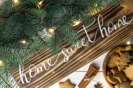 Home Sweet Home lettering burnt wood sign with gingerbread cookie, Christmas tree branches, cinnamon sticks and anise on white surface. Flat layの写真素材