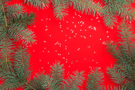 Branches of a Christmas tree on a red background with silver confetti stars. Merry christmas and happy new year concept. Flat lay. Copy space.の写真素材