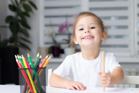 Cute little girl 2-4 in a white t-shirt draws at home with colorful felt-tip pens and pencilsの写真素材