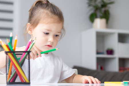 Cute little girl 2-4 in a white t-shirt draws at home with colorful felt-tip pens and pencilsの写真素材