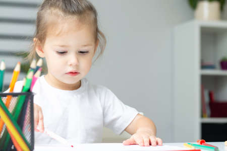 Cute little girl 2-4 in a white t-shirt draws at home with colorful felt-tip pens and pencilsの写真素材