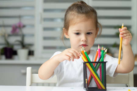 Cute little girl 2-4 in a white t-shirt draws at home with colorful felt-tip pens and pencilsの写真素材