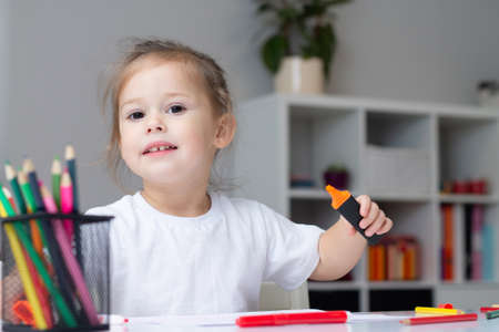 Cute little girl 2-4 in a white t-shirt draws at home with colorful felt-tip pens and pencilsの写真素材