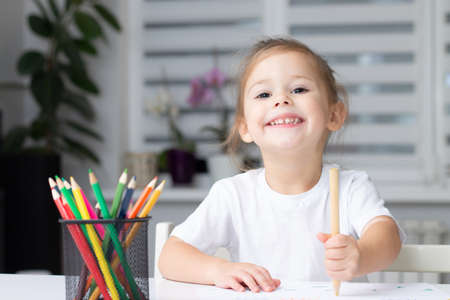 Cute little girl 2-4 in a white t-shirt draws at home with colorful felt-tip pens and pencilsの写真素材