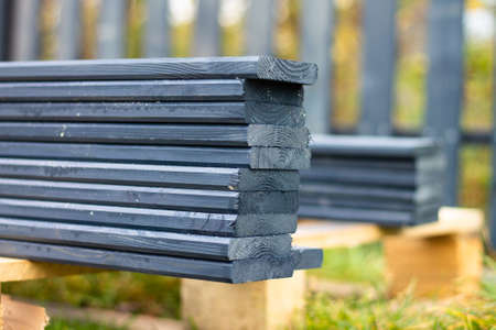 A dark gray painted fence boards stacked outside, partially blurred