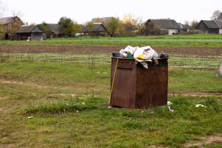 Overflowing rusty trash can in the countryside. Rubbish scattered on the ground. Environmental protection problemの写真素材