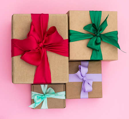 Gifts in craft paper with colorful ribbons on a pink background. Top view