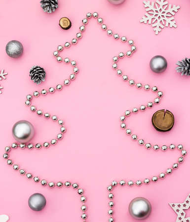 Christmas and New Year. Silhouette of a Christmas tree made of beads with Christmas toys and cones on a pink background. Flat lay. Copy spaceの写真素材