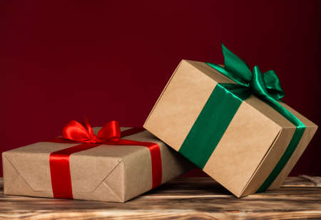 Gifts in craft paper with red and green ribbons on a dark red background. Copy spaceの写真素材
