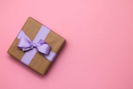 Gift in craft paper with lilac ribbon on a pink background. Top view. Copy spaceの写真素材