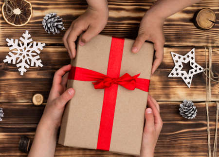 Hands giving or receiving a gift in craft paper with a red ribbon on rustic wood Christmas and New Year background. Top viewの写真素材