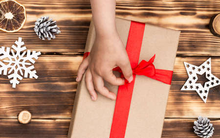 Hands giving or receiving a gift in craft paper with a red ribbon on rustic wood Christmas and New Year background. Top viewの写真素材