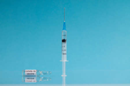 An ampoule with the COVID-19 coronavirus vaccine and a syringe stands against a blue background, copy spaceの写真素材
