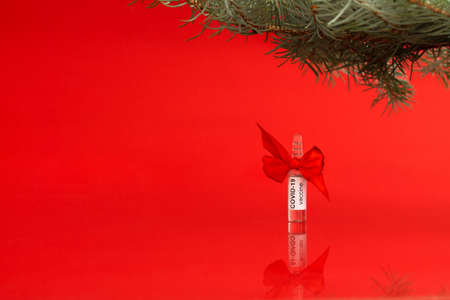 An ampoule of the COVID-19 coronavirus vaccine stands under a Christmas tree branch as a gift on a red background, copy spaceの写真素材