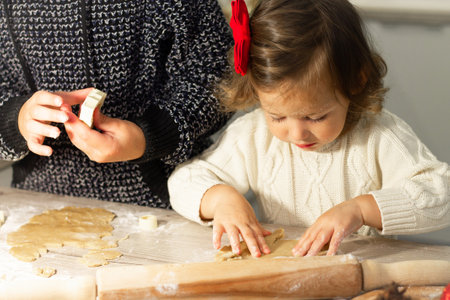 Cute little serious girl 2-4 with a red bow prepares Christmas gingerbread cookies in the New Year's kitchen.の写真素材