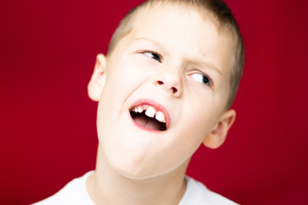 Boy teenager 7-10, shows a place from a lost tooth on a red backgroundの写真素材
