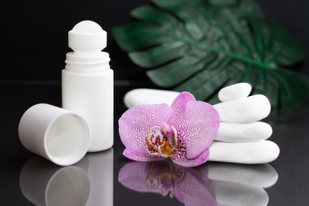Beautiful lilac orchid flower and white roll-on deodorant with white stones and monstera leaves, on black backgroundの写真素材
