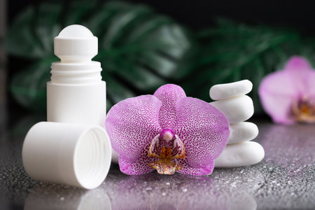 Beautiful lilac orchid flower and white roll-on deodorant with white stones and monstera leaves, on black wet backgroundの写真素材