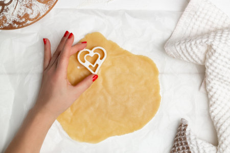 A woman's hand cuts heart-shaped cookies from rolled dough. Flat layの写真素材