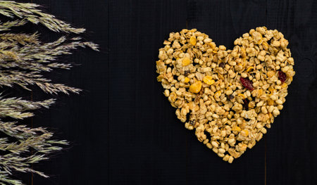 Heart laid out of granola and spikelets on a black wooden background. Flat lay. Copy space.の写真素材