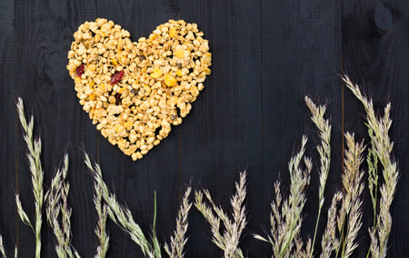 Heart laid out of granola and spikelets on a black wooden background. Flat lay. Copy space.の写真素材