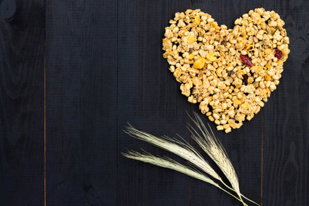 Heart laid out of granola and spikelets on a black wooden background. Flat lay. Copy space.の写真素材