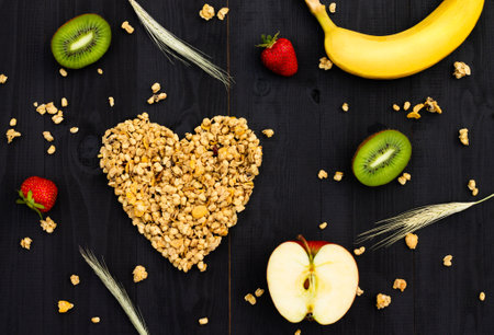 Heart laid out of granola, fruits and spikelets on a black wooden background. Flat lay.の写真素材