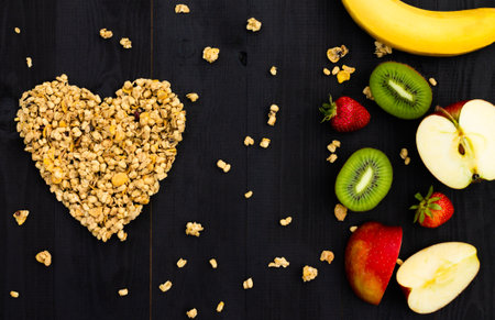 Heart laid out of granola and fruits on a black wooden background. Flat lay. Copy space.の写真素材