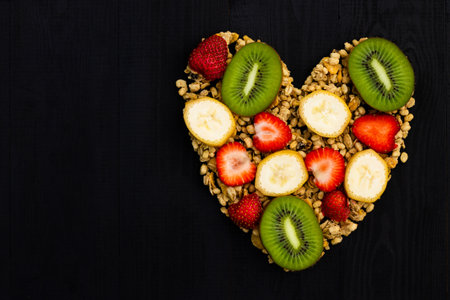 Heart laid out of granola and fruits on a black wooden background. Flat lay. Copy space.の写真素材