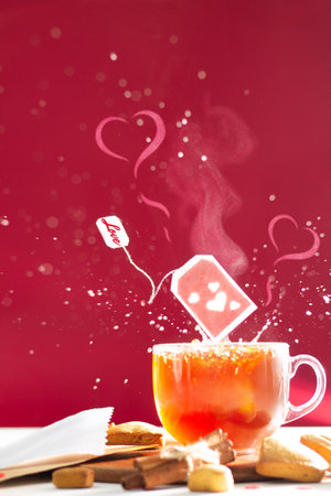 Tea bag with hearts and inscription Love on label above tea mug with splashes and heart shaped steam on dark red background. Copy spaceの写真素材