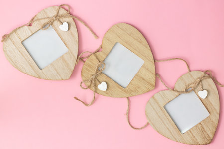 Three wooden heart-shaped photo frames on a pink background, flat lay, copy space.の写真素材