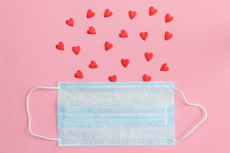 Protective face mask on pink background with red hearts. Flat lay. Copy space.の写真素材