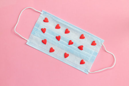 Protective face mask on pink background with red hearts. Flat lay. Copy space.の写真素材