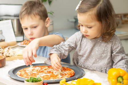 Cute little girl 2-4 in gray dress and boy 7-10 in T-shirt cooking pizza together in kitchen. Brother and sister cookingの写真素材