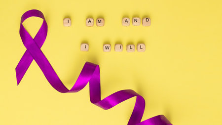 Wooden cubes with text of the slogan of World Cancer Day I am and I will and a purple ribbon, on a yellow surface. Flat lay. Bannerの写真素材