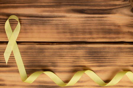 Yellow awareness ribbon, on wooden background. Sarcoma. Childhood cancer. World Cancer Day. Flat lay. Copy spaceの写真素材