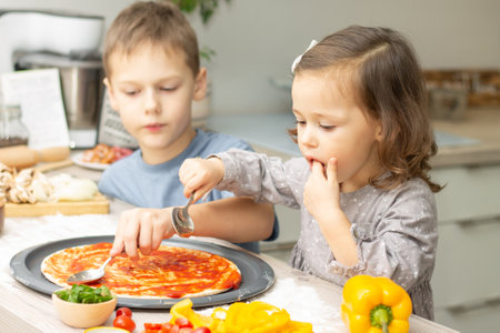 Cute little girl 2-4 in gray dress and boy 7-10 in T-shirt cooking pizza together in kitchen. Brother and sister cookingの写真素材