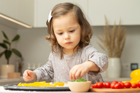 Cute little girl 2-4 in gray dress cooking pizza in kitchen. Kid arranges ingredients on pizza baseの写真素材