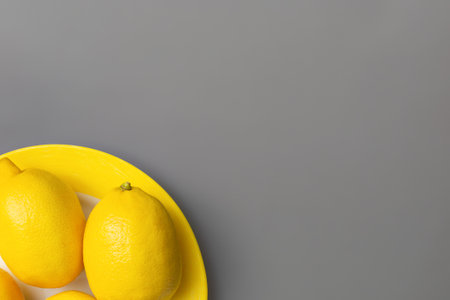Yellow lemons on yellow plate on gray background. Colors of the Year 2021 Illuminating and Ultimate gray. Flat lay. Copy spaceの写真素材