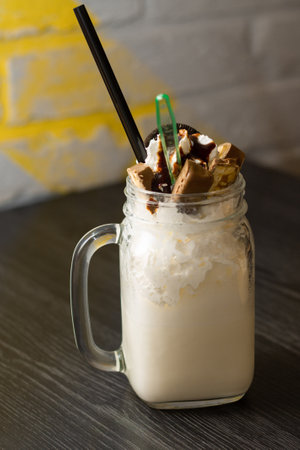 Freakshake in jar with cocktail straw, chunks of chocolate and cookies on dark wooden tableの写真素材