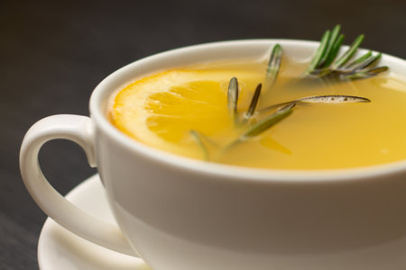 Yellow ginger tea with lemon and rosemary branch in white cup on wooden tableの写真素材