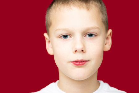 Boy teenager 7-10 in a white t-shirt, smiling on a red backgroundの写真素材