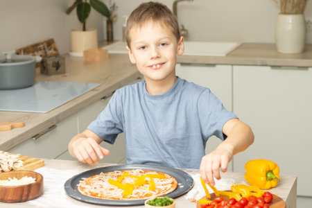 Boy 7-10 in T-shirt cooking pizza in kitchen. Kid smiles and cooksの写真素材
