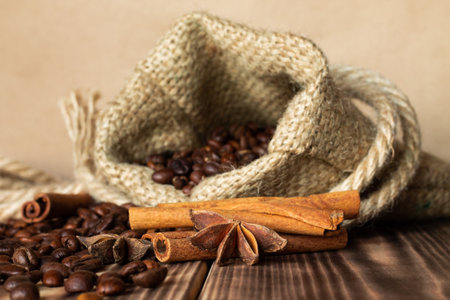 Coarse burlap sack with sprinkled grains of coffee on a burnt wood tabletop with cinnamon sticks and anise stars. Copy spaceの写真素材